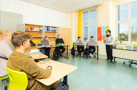 Jugendliche sitzen im Klassenzimmer, folgen der Lehrerin im Unterricht.